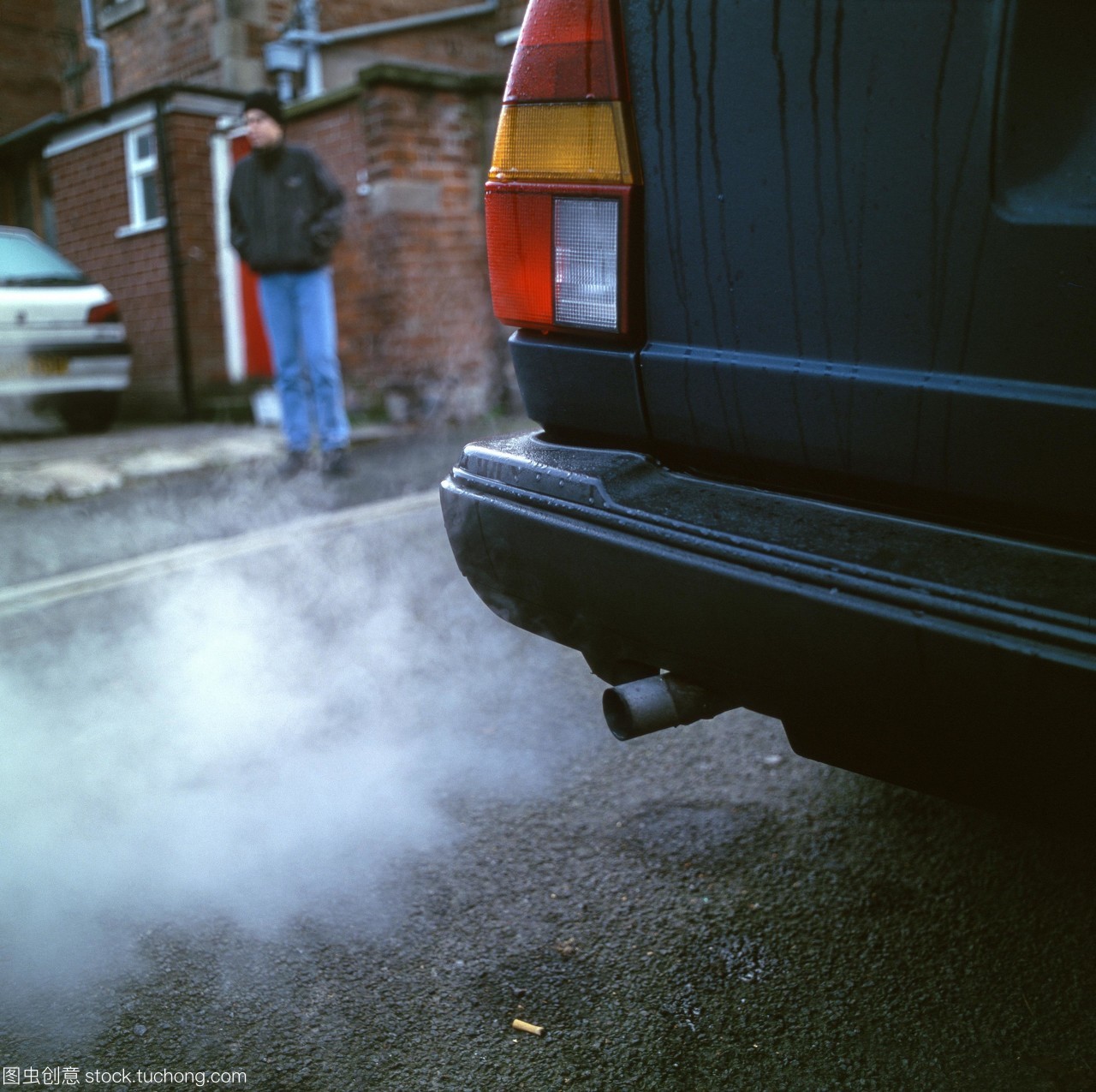 交通污染。汽车废气在市区与行人在人行道上。根据燃料的类型和发动机的设计,废气可以包含有毒气体,如一氧化碳,臭氧和氮氧化物。煤烟颗粒和未燃烧的碳氢化合物也会产生。交通废气是城市中主要的空气污染物。严重的空气污染与肺病的发病率有关。摄于英格兰西米德兰兹郡。